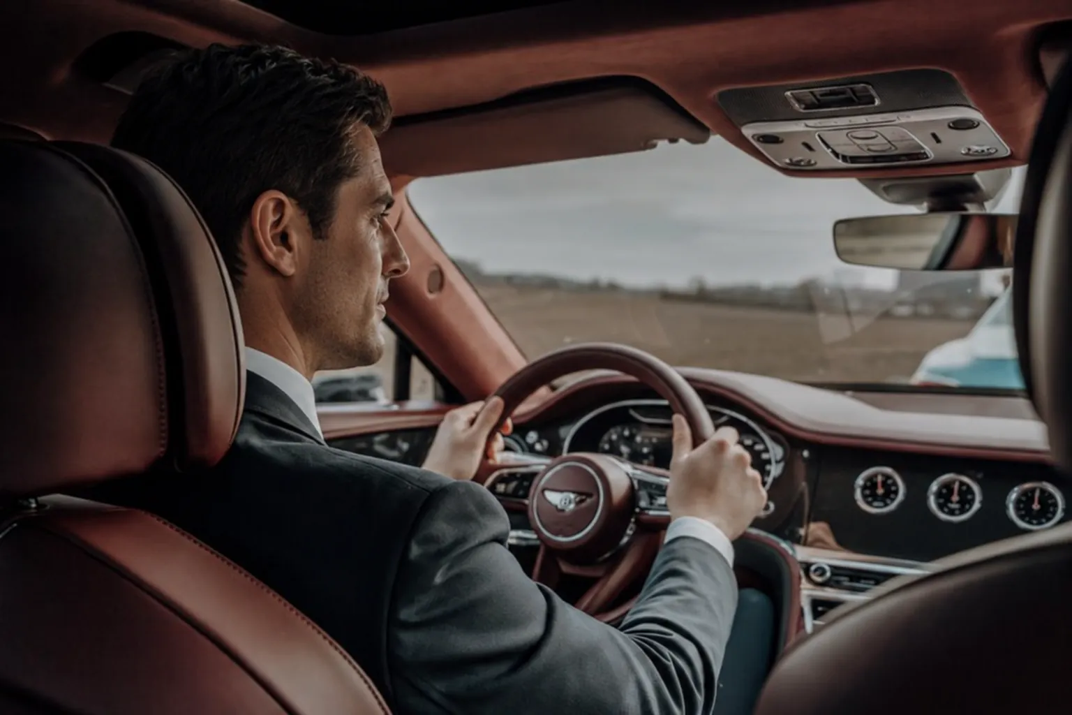 Chauffeur in a suit at the wheel, seen from the back seat of a Bentley